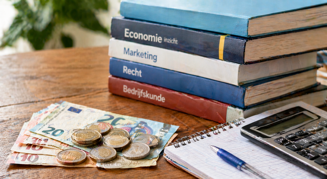 Foto: Geld, studieboeken, rekenmachine op tafel