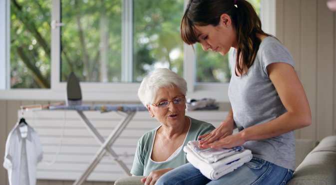 young woman helping senior lady with the housework Huishoudelijke hulp vouwt was op